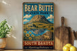 A vintage-style sign for Bear Butte State Park in South Dakota, featuring a mountain landscape with a lake and sunflowers.