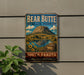 A vintage metal sign for Bear Butte State Park in South Dakota, featuring a mountain landscape with a lake and sunflowers.
