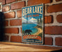 A vintage-style metal sign for Bear Lake State Park in Idaho, featuring a bear walking along a beach and mountains in the background.