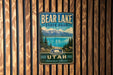 A metal sign with the text "BEAR LAKE STATE PARK UTAH Adventure Awaits" is displayed on a wooden wall.