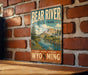 A vintage-style metal sign for Bear River State Park, featuring a scenic illustration of the river and mountains, mounted on a brick wall.