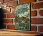 A vintage-style metal sign for Beaver Creek State Park in Ohio, featuring a scenic illustration of a covered bridge and waterfall.