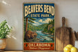 A vintage-style metal sign for Beaver Bend State Park, featuring an illustration of a beaver in a river surrounded by trees and mountains.