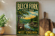 A vintage-style sign for Beech Fork State Park in West Virginia, featuring a scenic landscape with a river, forest, and cabin.