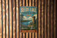 A vintage metal sign for Beeds Lake State Park in Iowa, featuring a castle, a lake, and a sailboat, is displayed on a wooden wall.