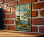 A vintage metal sign for Bellevue State Park in Delaware, featuring a scenic image of a lighthouse and a picnic table, mounted on a brick wall.