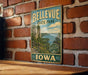 A vintage metal sign for Bellevue State Park in Iowa, featuring a scenic landscape with a river and mountains.