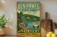 A vintage-style sign for Ben Hawes State Park in Kentucky, featuring a scenic landscape with a lake and mountains.