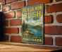 A vintage-style metal sign for Benjamin Rush State Park in Pennsylvania, featuring a scenic landscape with a lake and mountains.
