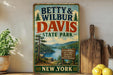 A vintage-style metal sign for Betty & Wilbur Davis State Park in New York, featuring a scenic landscape with a lake and mountains.