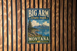 A vintage metal sign for Big Arm State Park in Montana, featuring a scenic landscape with mountains, a lake, and a pine tree.