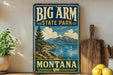 A vintage-style sign for Big Arm State Park in Montana, featuring a scenic landscape with mountains, a lake, and a sailboat.