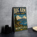 A vintage-style metal sign for Big Arm State Park in Montana, featuring a scenic landscape with mountains, a lake, and a sailboat.
