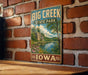 A vintage-style metal sign for Big Creek State Park in Iowa, featuring a scenic landscape with a river, trees, and flowers.