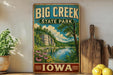 A vintage-style sign for Big Creek State Park in Iowa, featuring a scenic landscape with a lake, mountains, and flowers.
