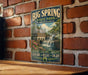 A vintage-style metal sign for Big Spring State Park in Pennsylvania, featuring a scenic image of a waterfall and a brick building.