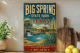 A vintage-style sign for Big Spring State Park in Texas, featuring a scenic illustration of a waterfall and a building, with the text "Big Spring State Park, Texas, Nature's Legacy, Est. 1933" displayed prominently.