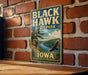 A vintage-style metal sign for Black Hawk State Park in Iowa, featuring a scenic landscape with a river, trees, and a bird in flight.