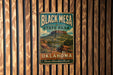 A vintage metal sign for Black Mesa State Park in Oklahoma, featuring a scenic mountain landscape.