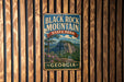 A vintage metal sign for Black Rock Mountain State Park in Georgia, featuring a scenic mountain landscape with pine trees and a blue sky.