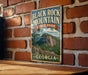 A vintage-style metal sign for Black Rock Mountain State Park in Georgia, featuring a scenic mountain landscape with pine trees and a prominent rock formation.