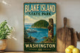 A vintage-style sign for Blake Island State Park in Washington, featuring a scenic image of the park and a boat on the water.
