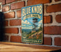 A vintage-style metal sign for Blue Knob State Park in Pennsylvania, featuring a scenic illustration of a lookout tower and mountains.
