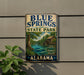 A vintage-style sign for Blue Springs State Park in Alabama, featuring a scenic illustration of the park's natural surroundings.