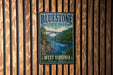 A vintage-style metal sign for Bluestone State Park, featuring a scenic image of a river and bridge, mounted on a wooden wall.