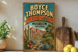 A vintage-style poster of Boyce Thompson Arboretum, a desert park in Arizona, is displayed on a wall next to a wooden cutting board and some potted plants.