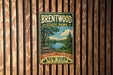 A vintage metal sign for Brentwood State Park, featuring a scenic landscape with a lake, trees, and a picnic table, mounted on a wooden wall.
