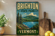 A vintage-style sign for Brighton State Park in Vermont, featuring a scenic landscape with mountains, trees, and a lake.