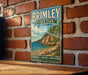 A vintage-style metal sign for Brimley State Park in Michigan, featuring a scenic landscape with a rocky cliff, trees, and a body of water.