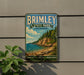 A vintage-style sign for Brimley State Park in Michigan, featuring a scenic landscape with a cliff overlooking a lake and pine trees.
