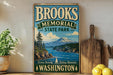 A vintage-style sign for Brooks Memorial State Park in Washington, featuring a scenic mountain landscape and a pine tree.