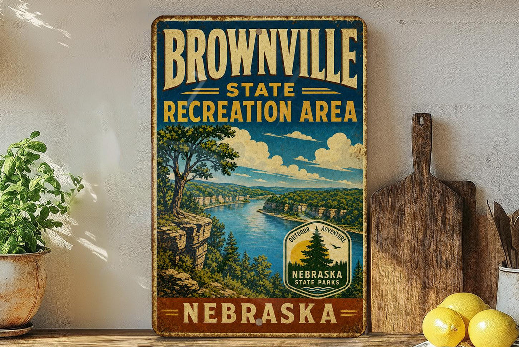 A vintage-style sign for the Brownville State Recreation Area in Nebraska, featuring a scenic landscape with a river, mountains, and a pine tree.