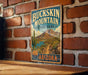A vintage-style metal sign for Buckkin Mountain State Park in Arizona, featuring a desert landscape with mountains, a cactus, and a path leading to the park.