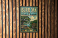A vintage metal sign for Burr Oak State Park in Ohio, featuring a scenic illustration of a river and trees.