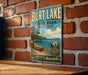 A vintage-style sign for Burt Lake State Park in Michigan, featuring a scenic image of a lake and a canoe, mounted on a brick wall.