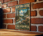 A vintage-style metal sign for Burton Creek State Park in California, featuring a scenic illustration of a river, mountains, and trees.