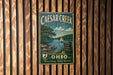 A vintage metal sign for Caesar Creek State Park in Ohio, featuring a scenic illustration of a lake, trees, and a sailboat.