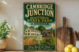 A vintage-style metal sign for Cambridge Junction Historic State Park in Michigan, featuring an illustration of a cabin and a dirt road.