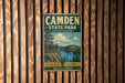 A vintage metal sign for Camden State Park in Minnesota, featuring a scenic landscape with a lake and mountains.