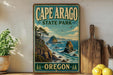 A vintage-style sign for Cape Arago State Park in Oregon, featuring a scenic coastal landscape with rocky cliffs, trees, and the ocean.