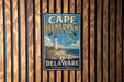 A vintage metal sign for Cape Henlopen State Park in Delaware, featuring a lighthouse and beach scene.