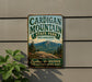 A vintage-style metal sign for Cardigan Mountain State Park in New Hampshire, featuring a scenic mountain landscape and the text "Explore, Discover, New Hampshire's Natural Beauty".