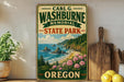 A vintage-style metal sign for Carl G. Washburne Memorial State Park in Oregon, featuring a scenic coastal landscape with rocky cliffs, a beach, and a body of water.