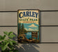 A vintage metal sign for Carley State Park in Minnesota, featuring a scenic landscape with pine trees, a lake, and mountains.