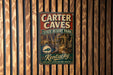 A vintage-style metal sign for Carter Caves State Resort Park in Kentucky, featuring a cave illustration and the text "Kentucky Nature's Wonderland Awaits".