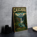 A vintage-style metal sign for Cascadia State Park in Oregon, featuring a waterfall and forest landscape, is displayed on a gray concrete surface.